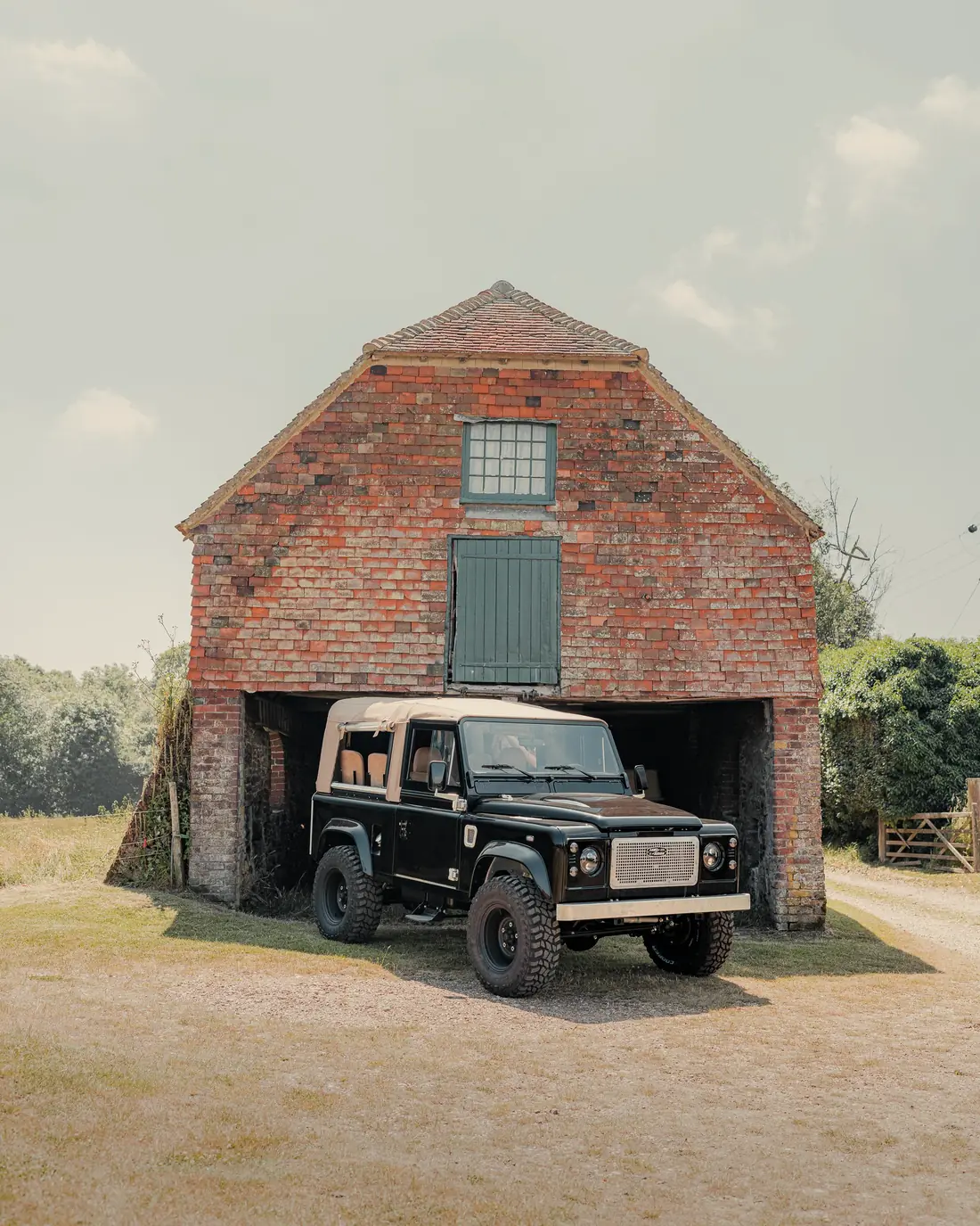 A Land Rover parked in the open cart shed of a brick and flint barn